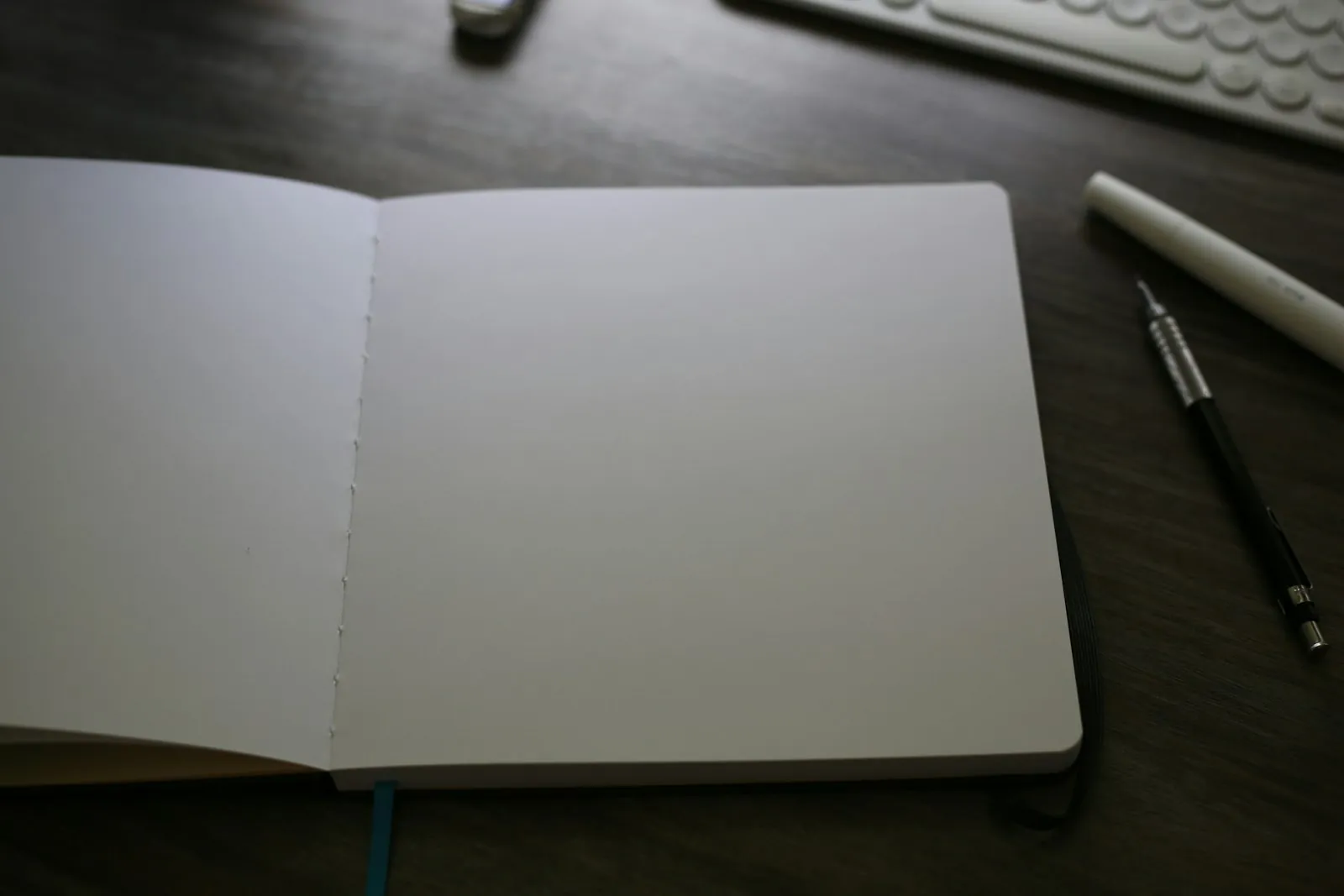 A real photograph of an open notebook, keyboard and writing tools on a desk.